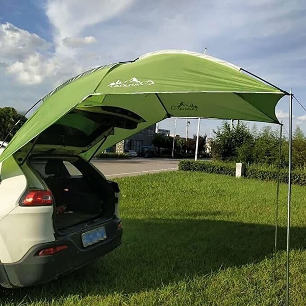 A green fabric awning attached to the rear of a car, creating a shaded outdoor living space in a grassy environment.
