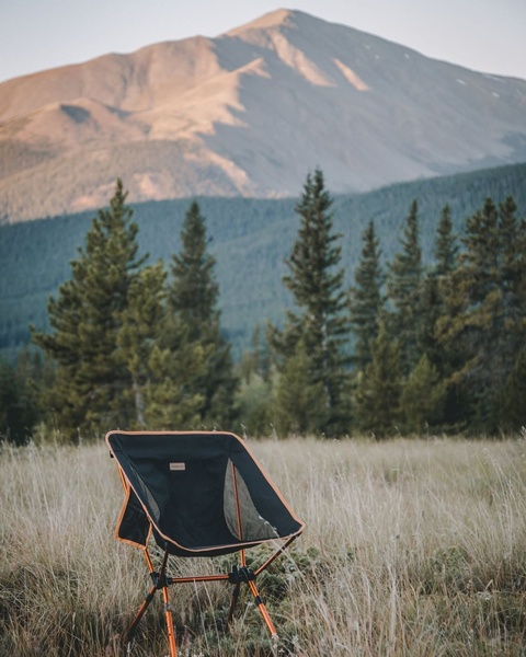 A high-quality 4:5 aspect ratio image featuring a portable camping chair set up in a vast mountain meadow.
